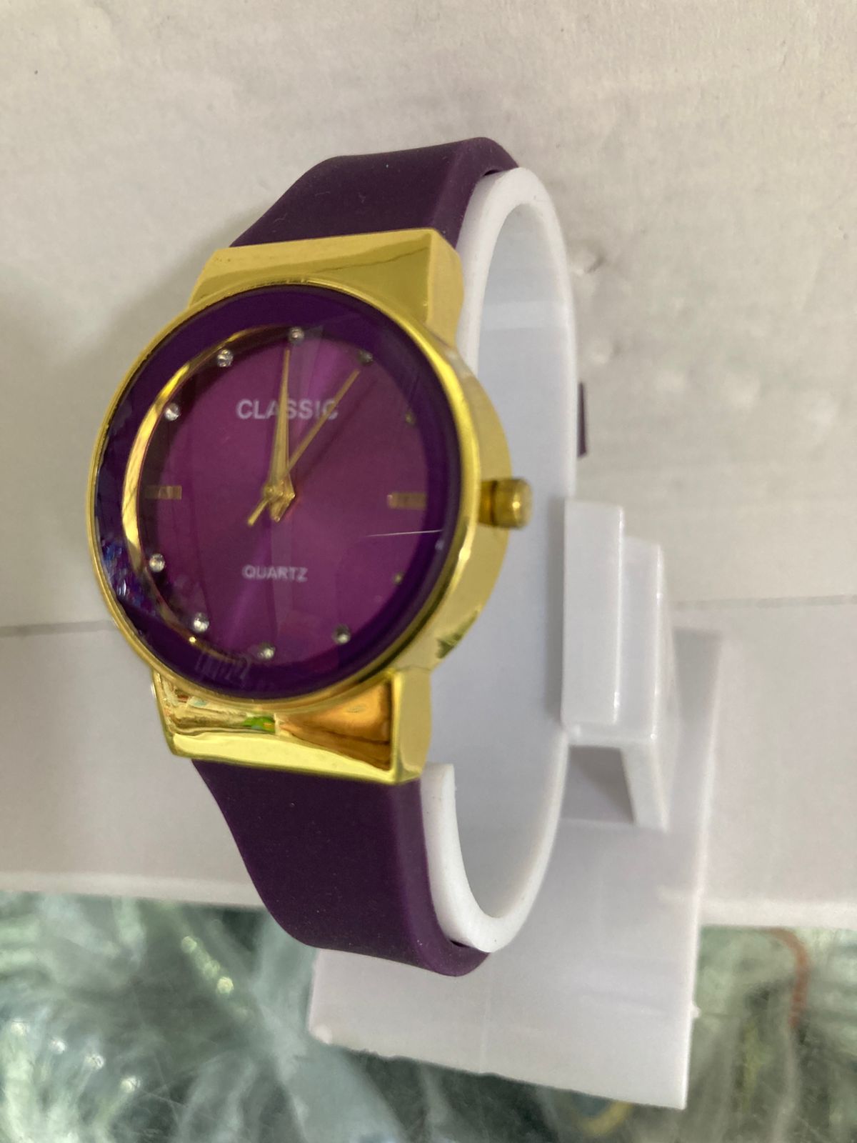 Watch with purple face and band on a white stand against a light gray background