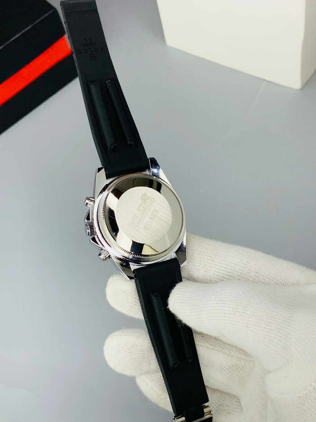 Watch with black strap held by a gloved hand on a gray background