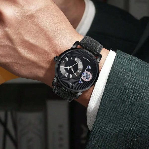 Black wristwatch with detailed face on a person's wrist, wearing a suit.