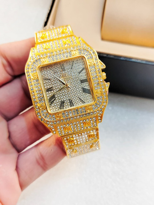 Gold diamond-encrusted watch held by a hand on a light background
