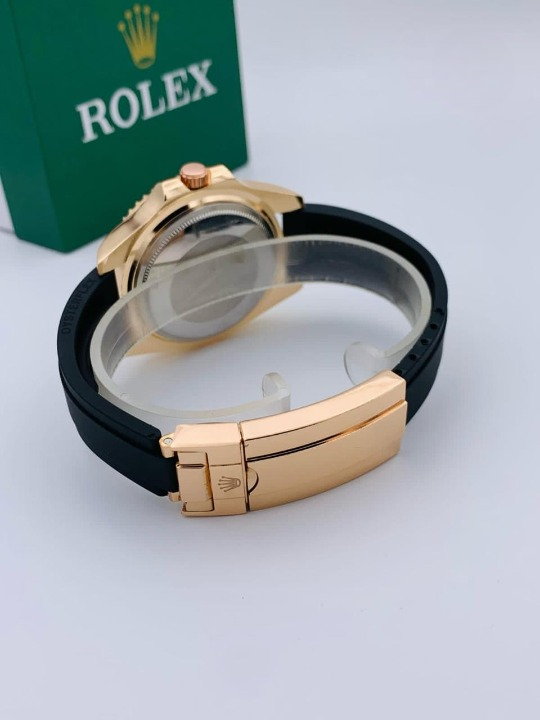 Gold watch with black strap on a white surface with a Rolex box in the background.