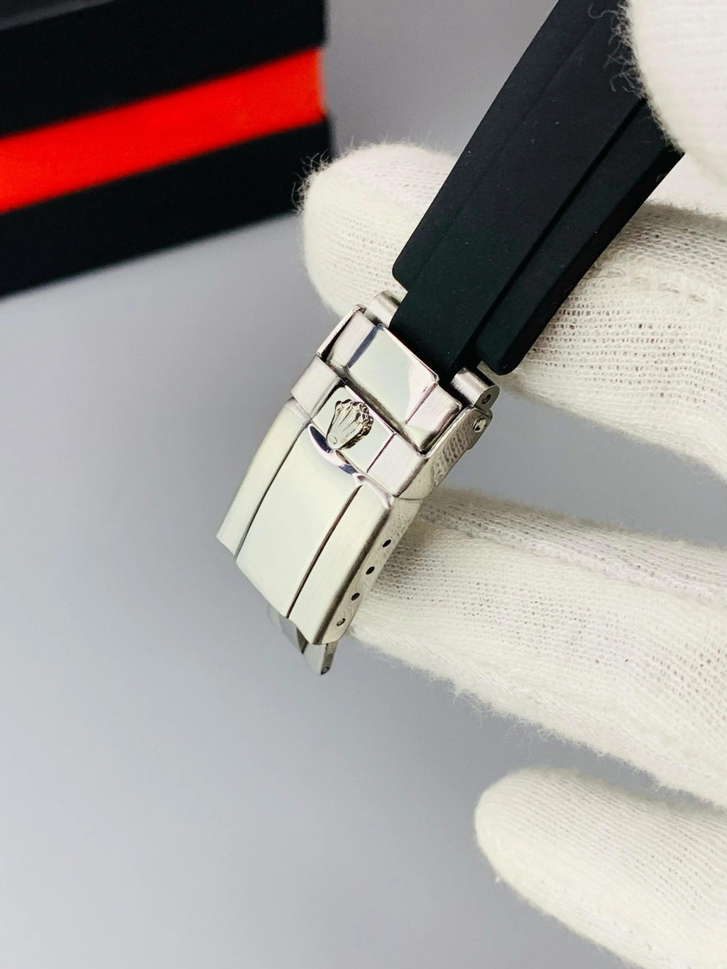 Close-up of a watch buckle with a brand logo on a gray background