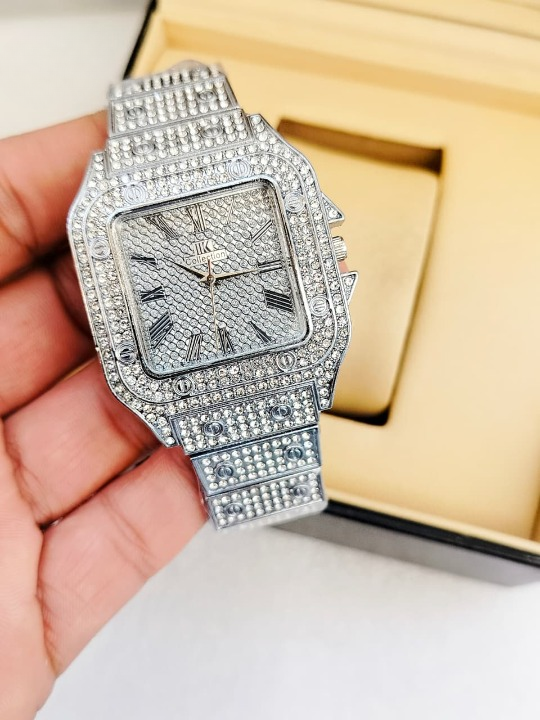 Luxury diamond-encrusted watch held in a hand with a gold box in the background.